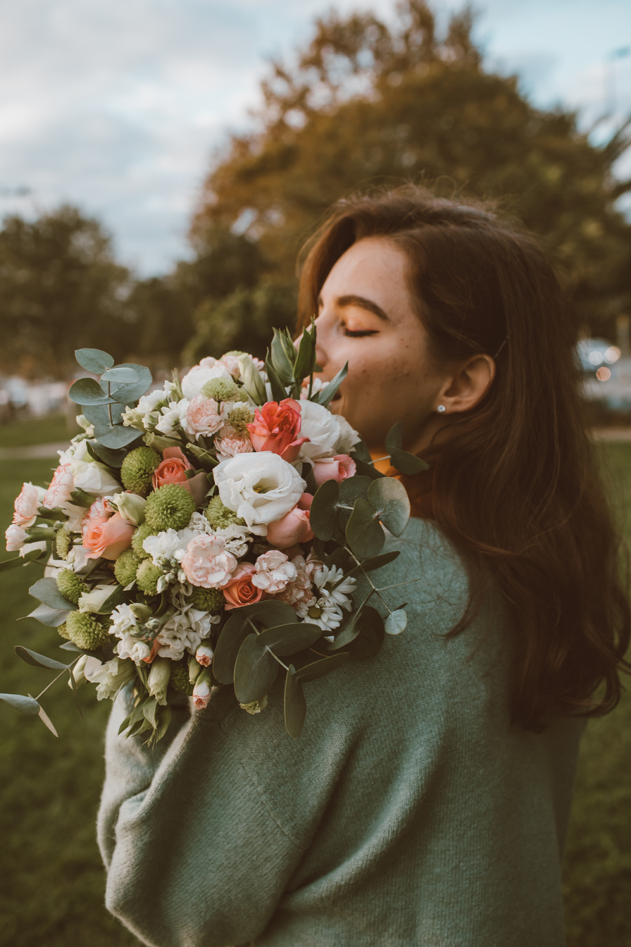 Woman in Green Sweater Holding a Bouquet of Flowers